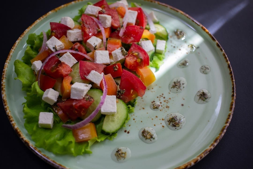 Bol cu salată grecească cu brânză feta, roșii, castraveți, ardei, ceapă roșie și măsline Kalamata, stropită cu ulei de măsline